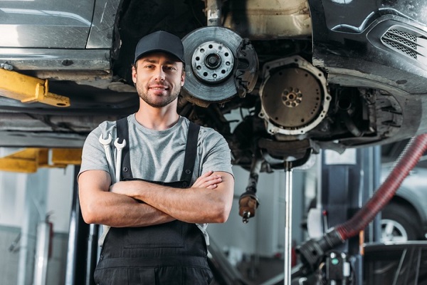 smiling workman posing with crossed arms in auto mechanic shop